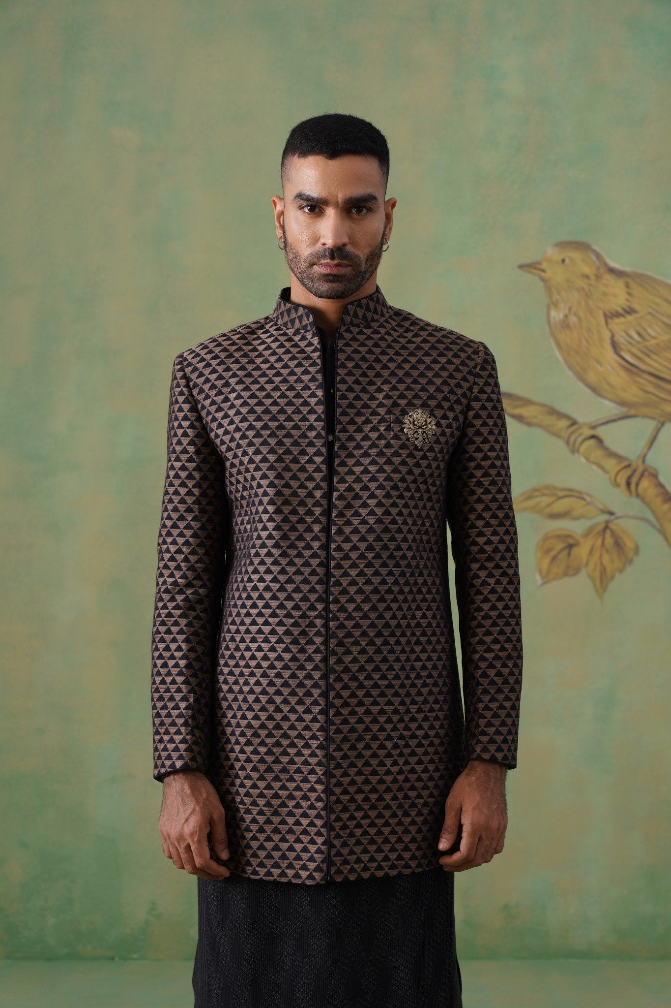 Man wearing a patterned jacket in front of a decorative wall with a bird design.